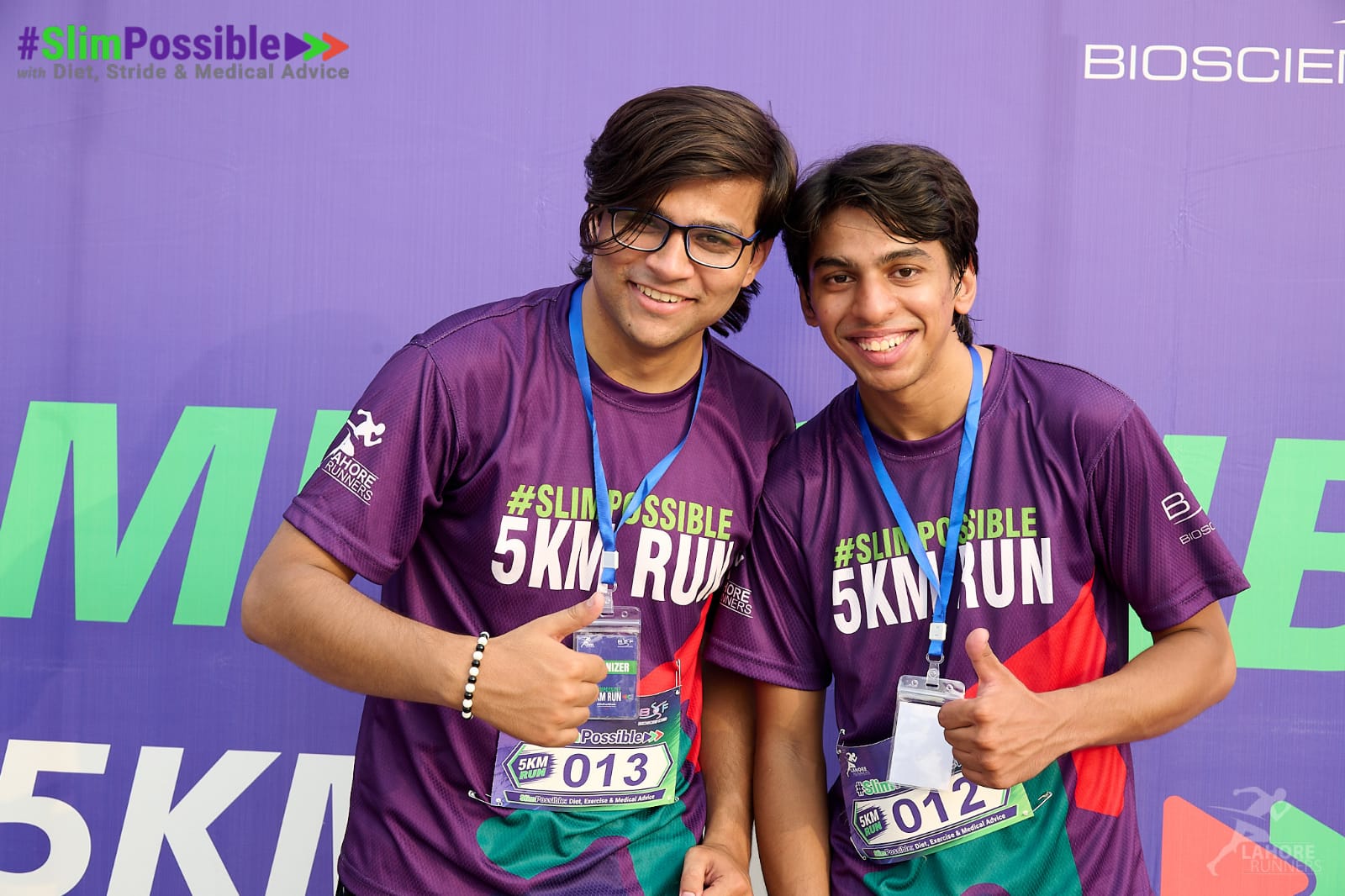 The two of us in purple #SlimPossible 5K shirts, bibs 013 and 012, giving thumbs up.